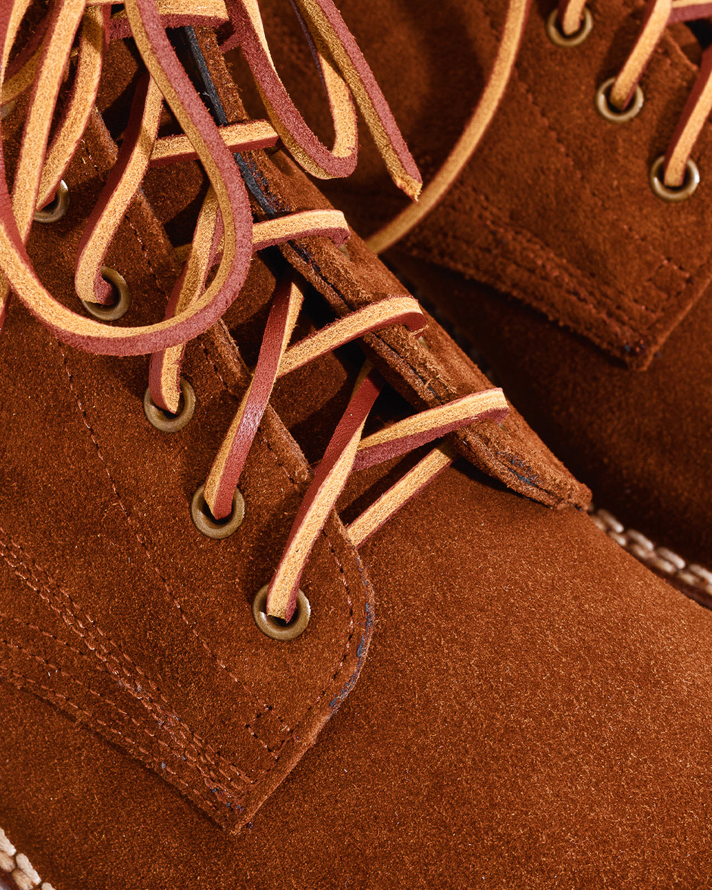 Close-up of a brown suede lace-up boot with tan and burgundy laces threaded through brass eyelets.