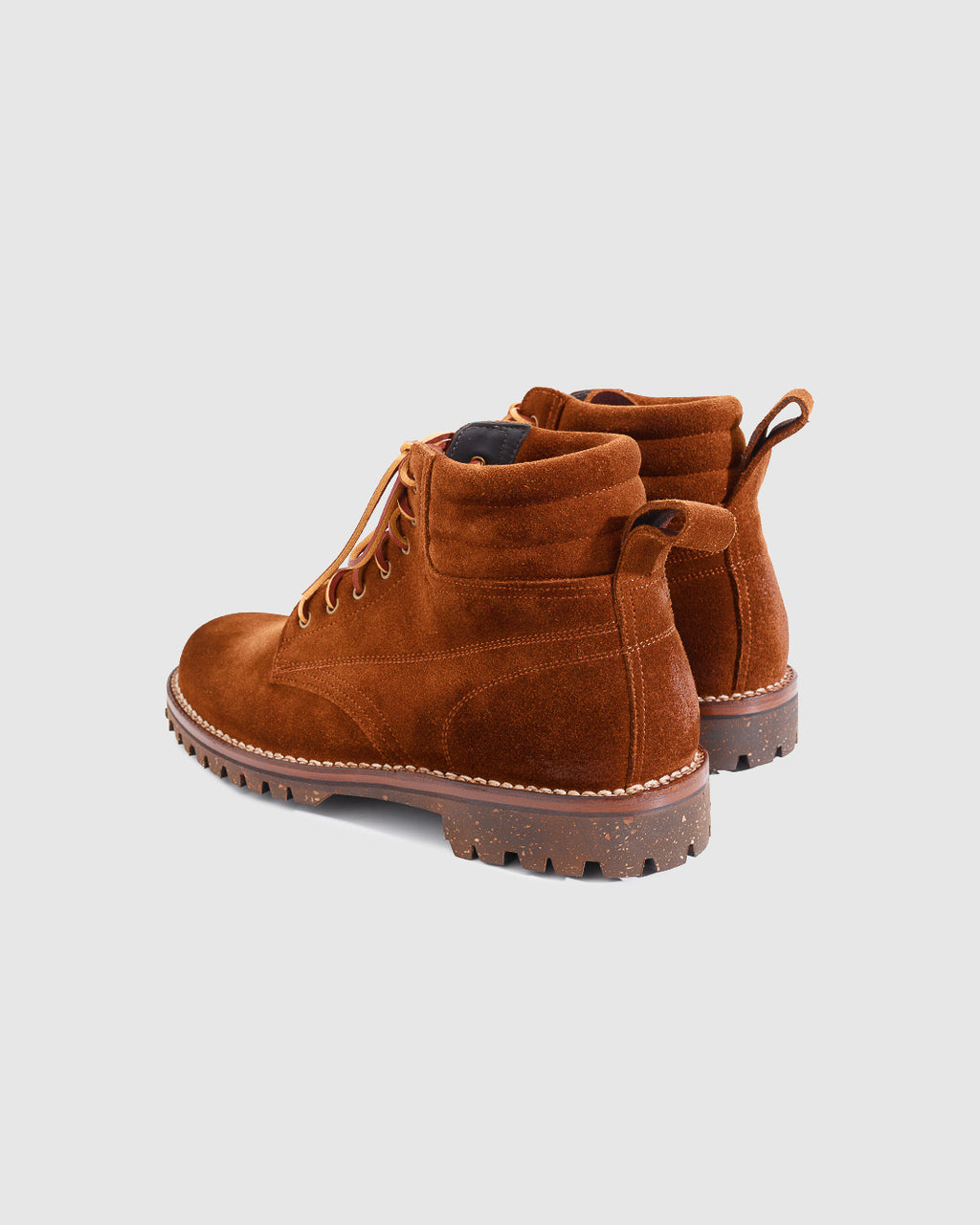 A pair of brown suede lace-up ankle boots with rugged lug soles, shown from a three-quarters rear angle on a light gray background.