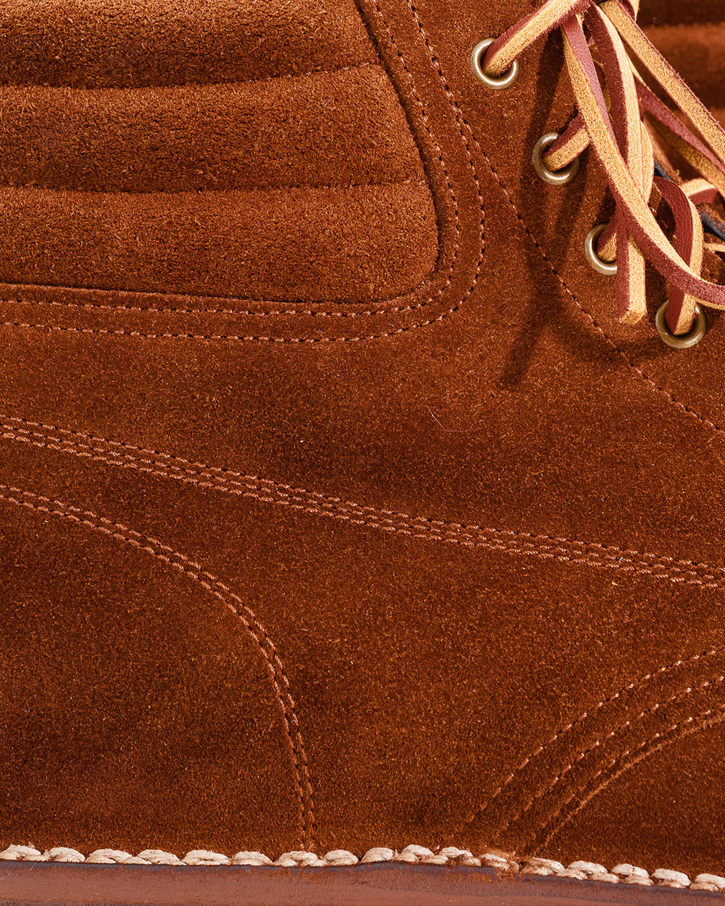 Close-up of a brown suede boot showing the textured material, stitching, eyelets, and part of the laces.